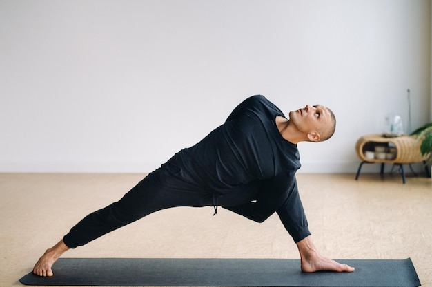 Мужчина в черной спортивной одежде занимается растяжкой йоги в спортзале