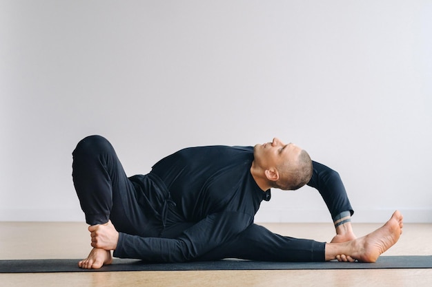 A man in black sportswear is doing Yoga stretching in the gym