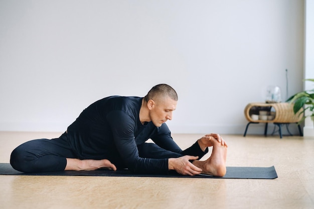 A man in black sportswear is doing Yoga stretching in the gym