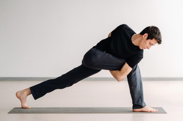 a man in a black t-shirt trains standing up, doing stretching in the gym