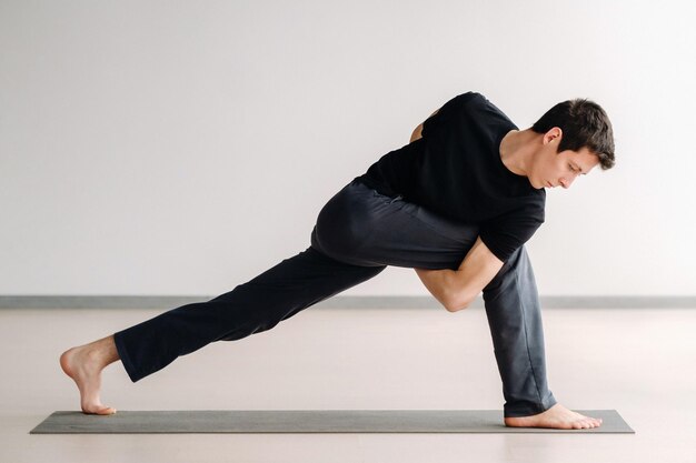 A man in a black T-shirt trains standing up, doing stretching in the gym