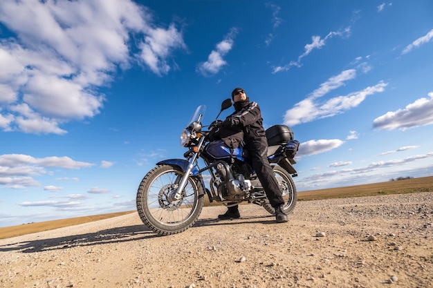 フィールドのパノラマと青空のオートバイの旅行の概念を背景に自転車で黒い制服を着た男