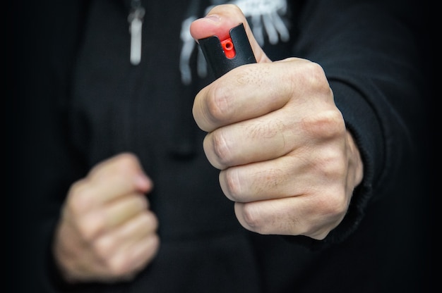 A man in black uniforms and gloves a tear gas or pepper spray. Means of self-defense. gas cartridge, gas canister