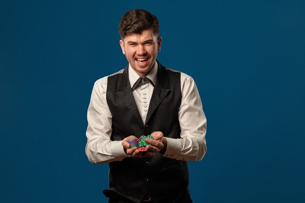 Man in black vest and trousers white shirt holding some colored chips