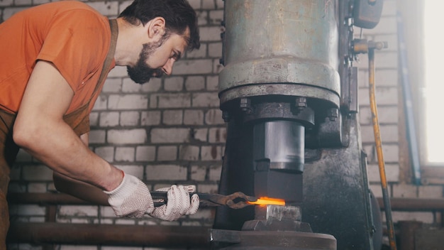 Man blacksmith forges the metal at the mechanical hammer - small business