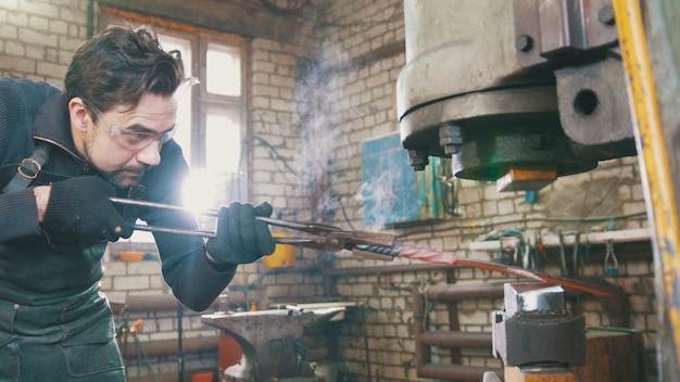 Photo man blacksmith in workshop forging red hot iron on anvil  small business