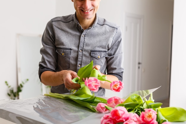 Man bloemist maakt rode tulpenboeket en verpakt in verpakking op houten tafel. Bloemen