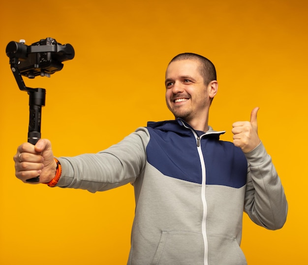 Man blogger video maken en duimen opdagen in de camera op gimbal op oranje achtergrond