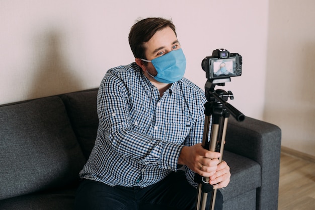 Man blogger wearing protective face mask is recording video on video camera. Male blogger streaming about coronavirus pandemic.