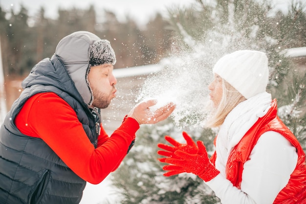 Man blowing snow from hand, woman has good sense of humor, winter holiday mood, couple have fun. Happy people, Valentines day, pampering