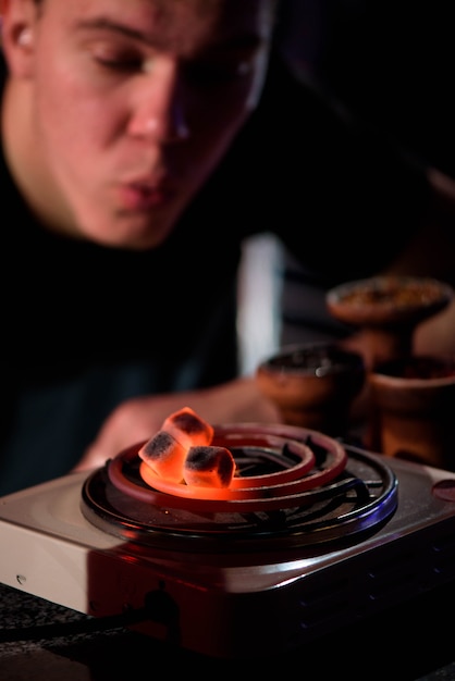 Man blows red hot coals for shisha hookah