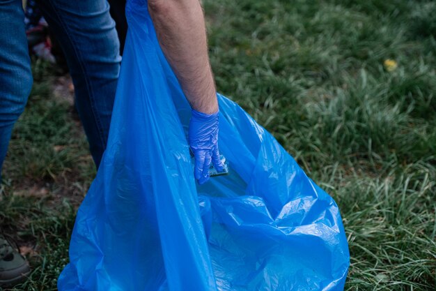 Man in blue gloves collects garbage in a blue bag