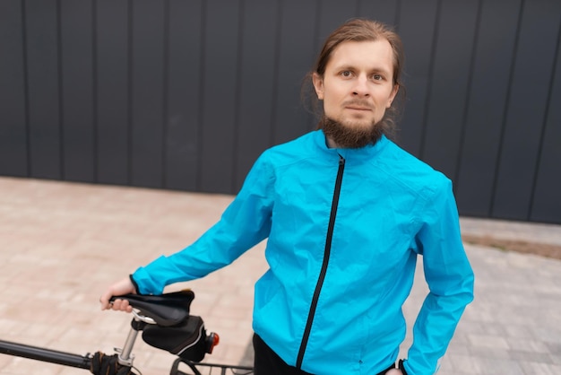 Мужчина в синей куртке держит велосипед и смотрит в камеру. Высококачественное фото.