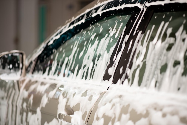 A man in a blue jacket and sunglasses washes his car at a\
selfservice car wash