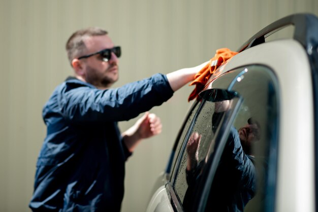 Un uomo con una giacca blu e occhiali da sole lava la sua auto in un autolavaggio self-service