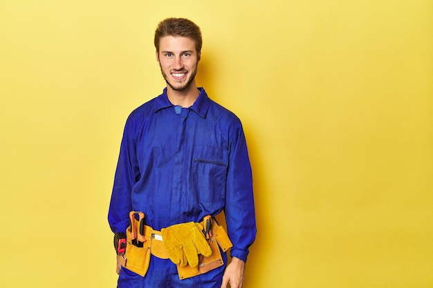 Man in blue jumpsuit with toolbelt on yellow happy smiling and cheerful