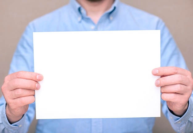 Foto un uomo in camicia blu, uomo d'affari che tiene foglio bianco bianco. spazio per testo, mockup