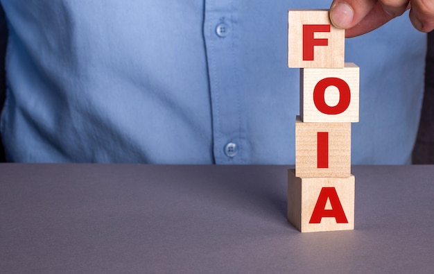 A man in a blue shirt composes the word FOIA The Freedom of Information Act from wooden cubes vertically