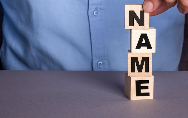 A man in a blue shirt composes the word NAME from wooden cubes vertically