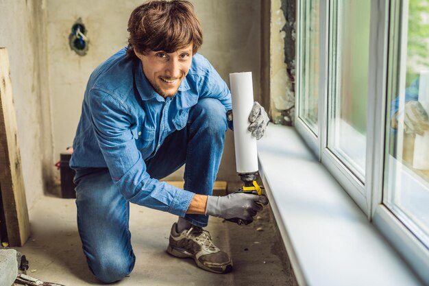 Man in a blue shirt does window installation. Using a mounting foam.