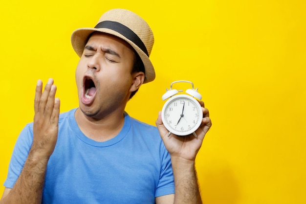 Man blue shirt holding alarm clock with a shocked expression on a yellow background