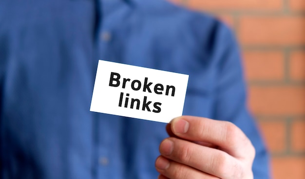 A man in a blue shirt holds a sign with the text of broken links audit in one hand