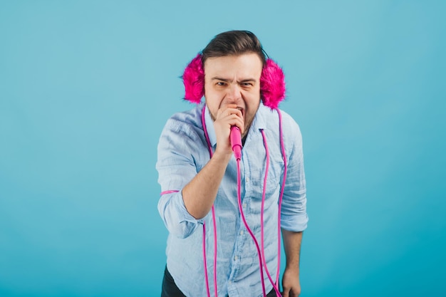 man in blue shirt stands on blue background in pink headphones and sings in pink microphone