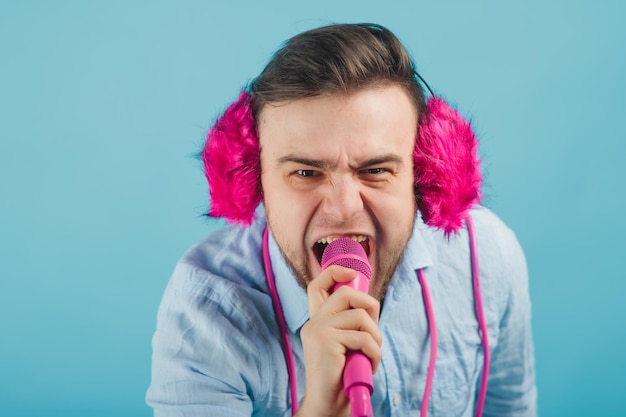 man in blue shirt stands on blue background in pink headphones and sings in pink microphone
