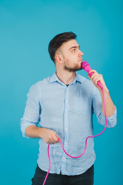 man in blue shirt stands on blue background and sings in pink microphone