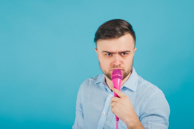 man in blue shirt stands on blue background and sings in pink microphone