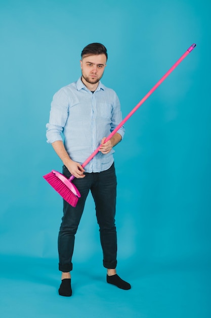 man in blue shirt stands on blue background with pink broom