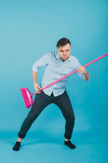 man in blue shirt stands on blue background with pink broom