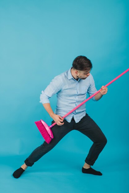 man in blue shirt stands on blue background with pink broom