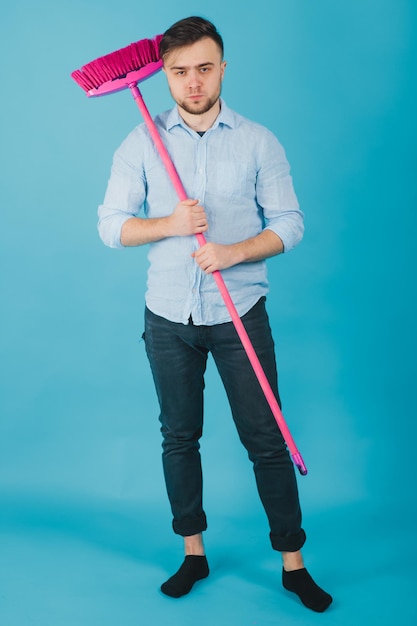 man in blue shirt stands on blue background with pink broom