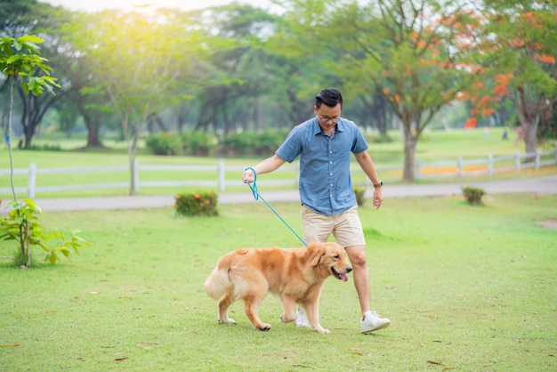 庭のゴールデンレトリーバー犬を歩く青いシャツの男