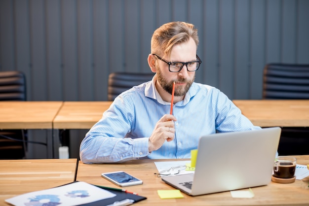 Man in blue shirt working with laptop at the modern office interior