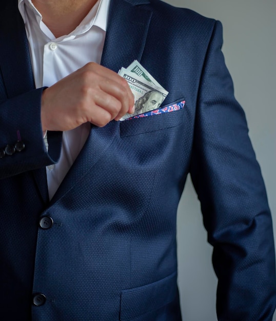 A man in a blue suit puts dollar bills in his pocket the concept of corruption