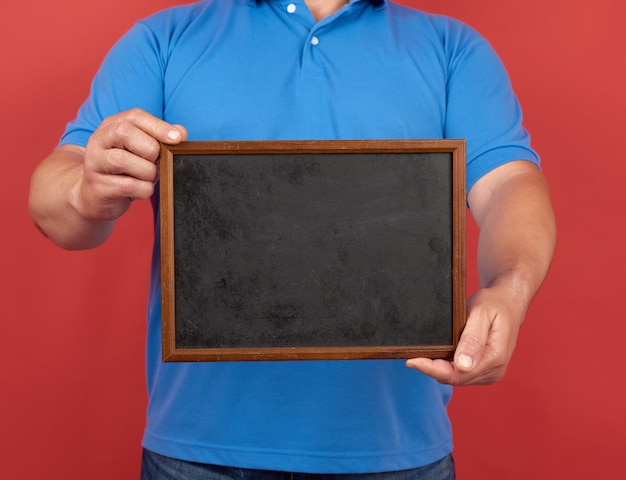 Man in a blue T-shirt holds an empty rectangular wooden frame for writing text