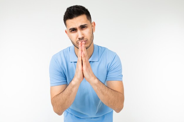 Man in a blue T-shirt prays on a white studio background