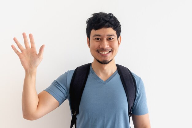 Man in blue t-shirt with backpack is waving hand isolated.