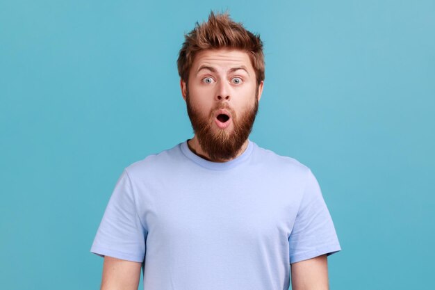 Man in blue Tshirt gasps from wonder holds breath stares at something horrible keeps mouth opened