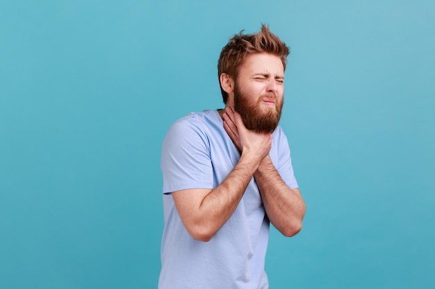 Man in blue Tshirt grimacing touching his neck feeling pain while swallowing sore throat