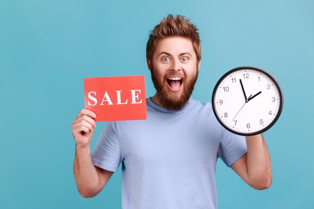 Man in blue Tshirt holding clock and card with sale inscription announcing finishing huge discounts