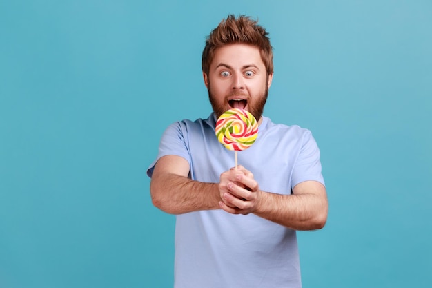 Man in blue Tshirt holding out sweet sugary confectionery feels hungry enjoying tasty lollipop