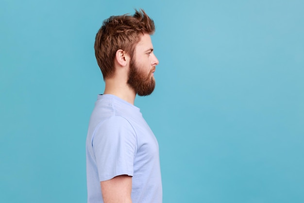 Man in blue Tshirt looking to side space with serious attentive face unsmiling determined male