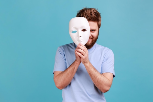 Man in blue Tshirt removing white mask from face showing his smiling expression good mood