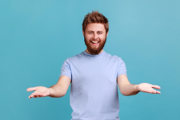 Man in blue Tshirt sharing opening hands looking at camera with kind smile greeting and regaling