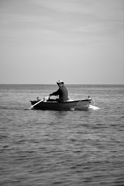 A man in a boat with a hat on is rowing a boat.