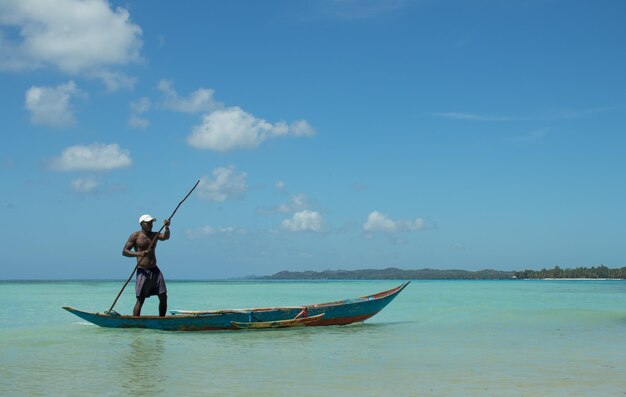 A man in a boat with a stick on his head is rowing in the ocean