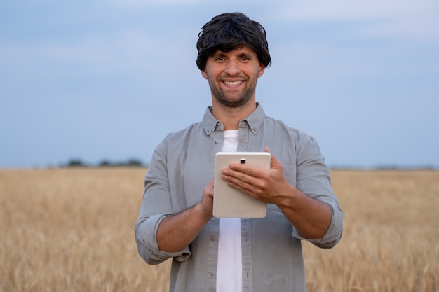 Man boer met behulp van digitale tabletcomputer die in een tarweveld staat en apps gebruikt en kwali...